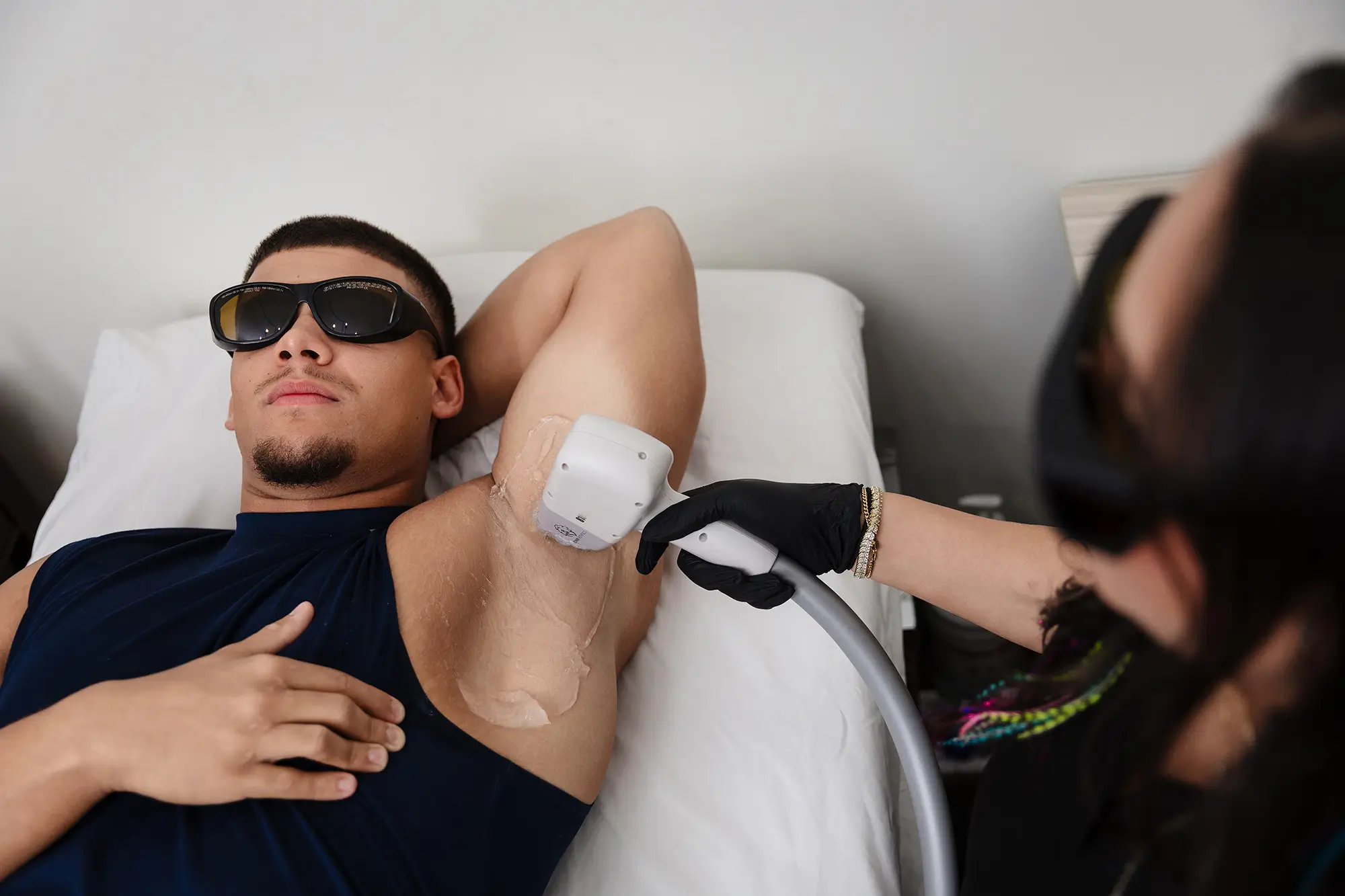 Man in protective eyewear relaxing while a specialist treats his underarm with laser hair removal
