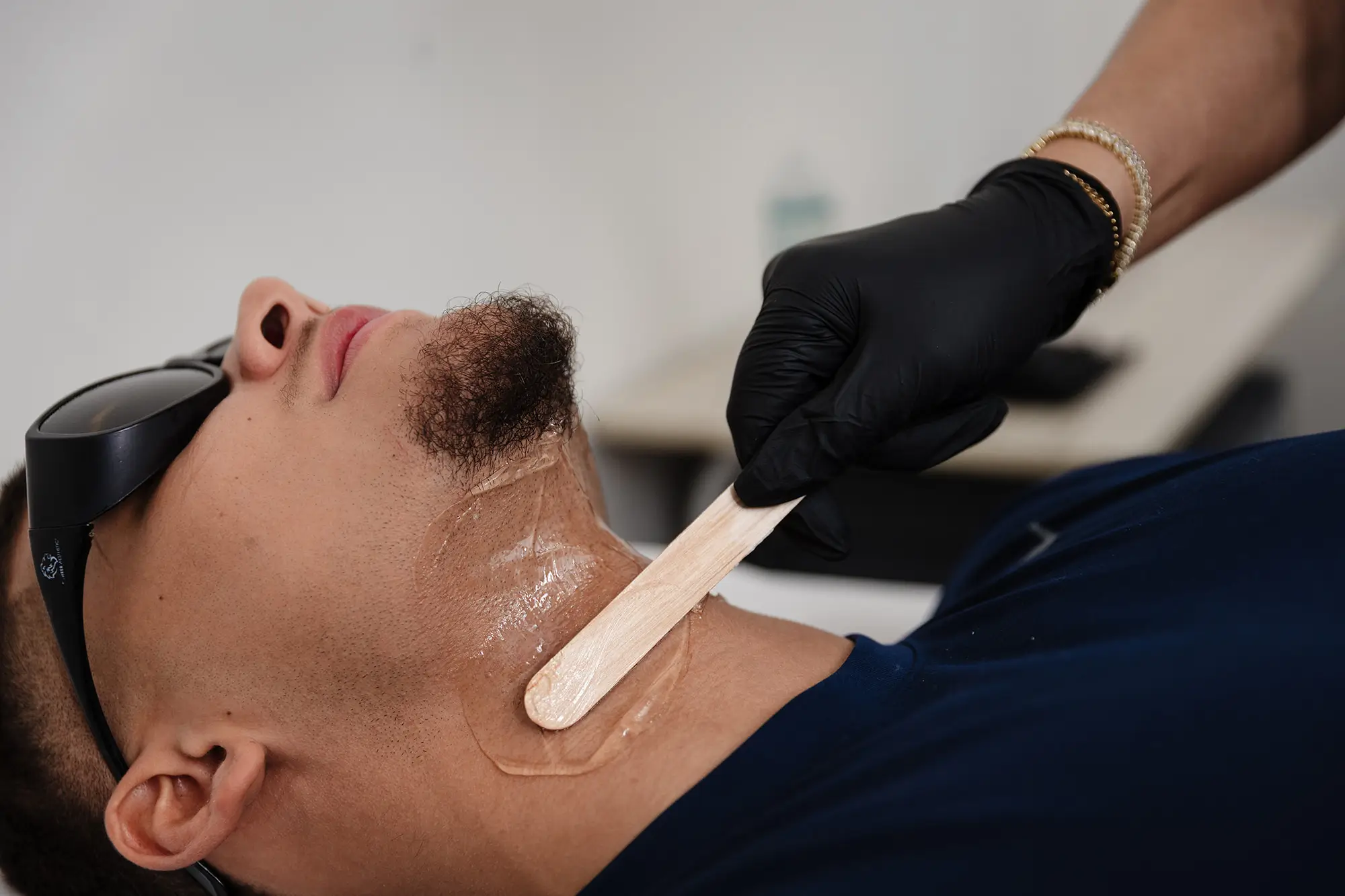 Provider in black gloves spreading cooling gel along a client's jaw and neck before laser hair removal