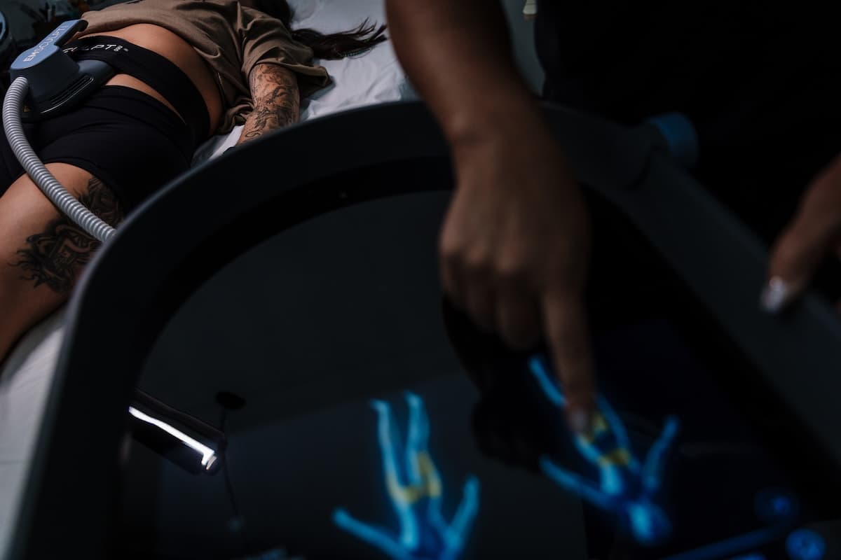 Provider adjusting EMSCULPT NEO settings on the treatment console while a client rests with an applicator secured to her hip