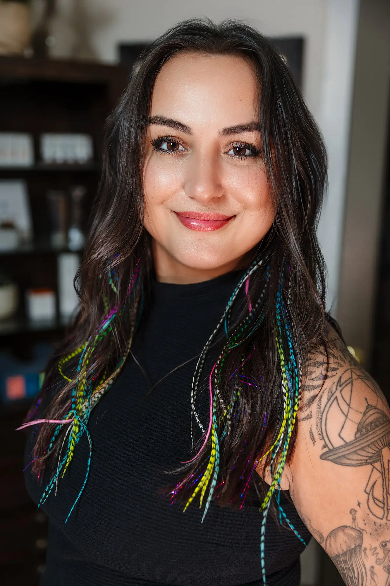 Nina, laser specialist at Wichita Laser Clinic, smiling with colorful hair feathers and a sleeve tattoo