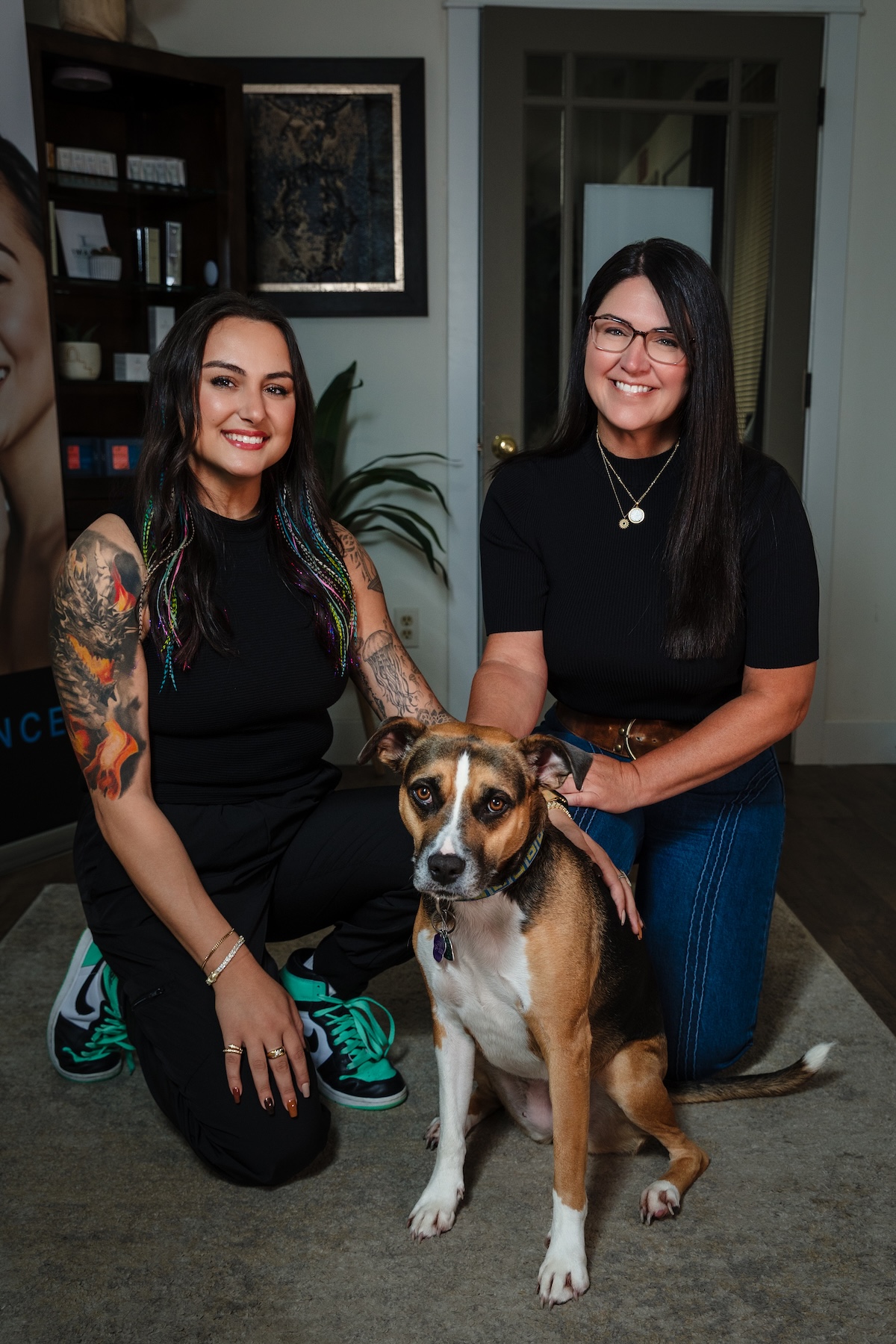 Nina and Stephanie of Wichita Laser Clinic kneeling in the clinic lobby with Luna, the office dog